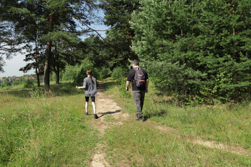 Teen girl and her dad enjoying quiet meadow walk, surrounded by vibrant green fields and pine trees, reconnecting through simple moments, nature escape from everyday life.