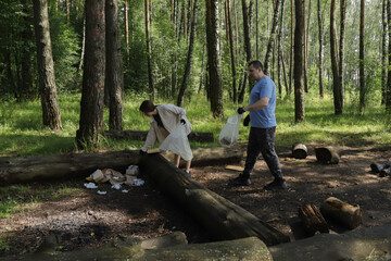Young couple taking part in forest preservation activity, removing trash from woodland picnic site with reusable bags, teamwork and responsible tourism in natural environment, sustainability in action