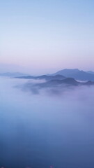 Fototapeta premium Tranquil mountain landscape covered in soft morning mist, blue and purple tones, peaceful dreamy nature scenery for vertical mobile wallpaper or digital mindfulness background