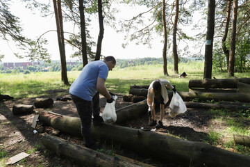 Man and young girl involved in forest preservation, encouraging family participation in green causes, collecting litter at former campfire site, promoting healthy lifestyle and eco-education.