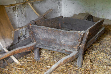 Old wooden farm wheelbarrow in a rural barn on a straw-covered floor. Traditional agricultural tool, rustic atmosphere, vintage countryside
