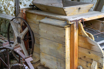 Old wooden threshing machine with wheels and mechanical drive, displayed against a rural building backdrop.