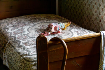 Old wooden bed with a patterned bedspread and a retro-style doll in a rural interior. Nostalgic atmosphere, traditional bedroom, vintage childhood.