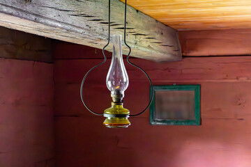 Vintage kerosene lamp hanging from a wooden ceiling in an old rural interior. Red log walls and...
