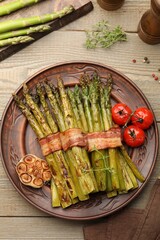 Tasty cooked asparagus served with bacon and spices on wooden table, flat lay