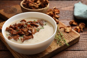 Tasty cream soup with mushrooms and thyme in bowl on wooden table, closeup