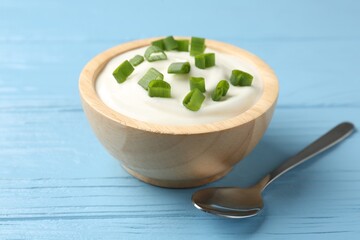 Tasty yoghurt with green onions in bowl on light blue wooden table, closeup