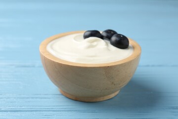 Tasty yoghurt with blueberries in bowl on light blue wooden table, closeup