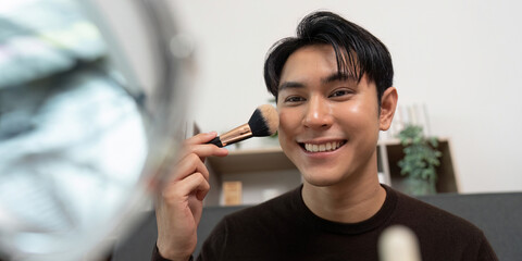 Makeup Application. Young man applying foundation with a brush in front of a mirror.