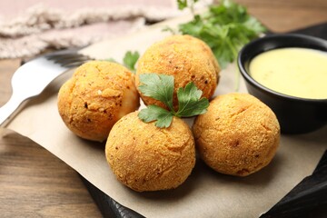 Delicious fried croquette balls with parsley and sauce on wooden table, closeup