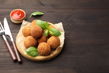 Delicious fried croquette balls with basil, cutlery and ketchup on wooden table. Space for text