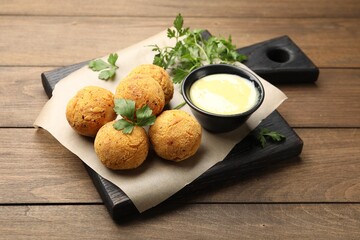 Delicious fried croquette balls with parsley and sauce on wooden table, closeup