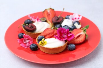 Sweet tartlets with berries and flowers on grey table, closeup. Delicious dessert
