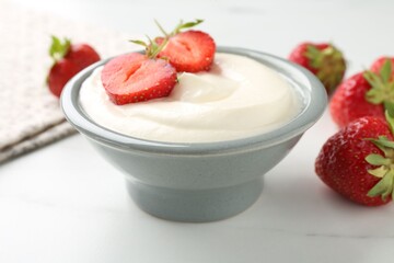 Delicious yogurt in bowl and strawberries on white marble table, closeup
