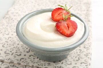 Delicious yogurt in bowl and strawberries on table, closeup