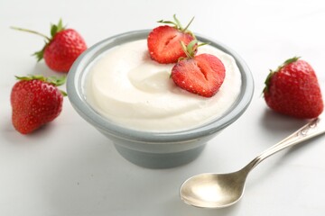 Delicious yogurt in bowl, strawberries and spoon on white table, closeup