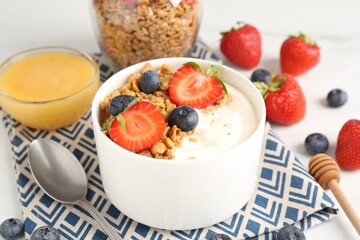 Tasty yogurt with granola, berries and honey on table, closeup