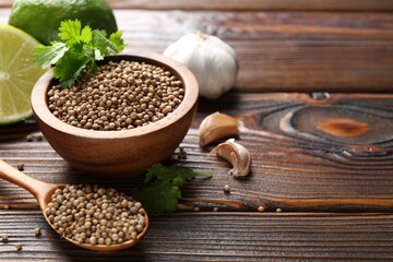 Coriander seeds, fresh cilantro, lime and garlic on wooden table, closeup. Space for text