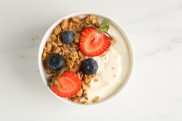 Tasty yogurt with granola and berries on white marble table, top view
