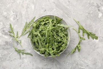 Fresh ripe green arugula leaves in bowl on grey table, flat lay