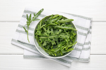 Fresh ripe green arugula leaves in bowl on white wooden table, top view