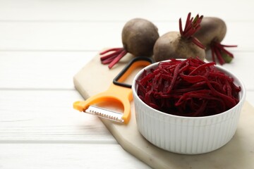 Raw beetroot noodles, fresh vegetables and peeler on white wooden table, closeup. Space for text