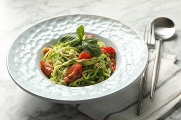 Tasty zucchini noodles with tomatoes, pine nuts and basil served on white marble table, closeup