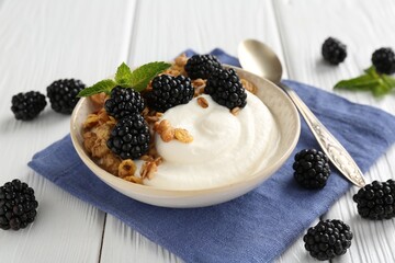 Tasty yogurt with granola and blackberries in bowl on white wooden table, closeup
