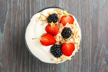 Tasty yogurt with granola and berries in bowl on wooden table, top view
