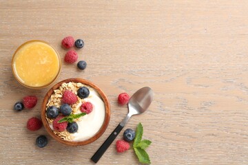 Tasty yogurt with granola, honey and berries in bowl on wooden table, flat lay. Space for text