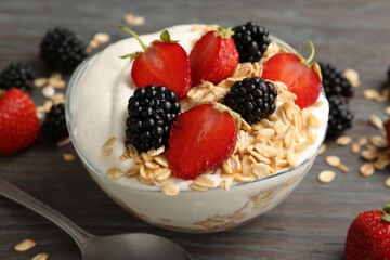 Tasty yogurt with granola and berries in bowl on wooden table, closeup
