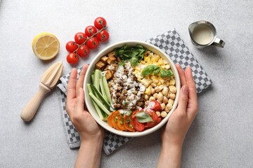 Healthy vegetarian food. Woman with delicious Buddha bowl at light grey table, top view
