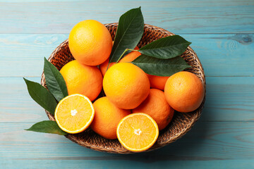 Fresh oranges and leaves in wicker basket on light blue wooden table, top view