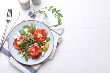 Tasty salad with arugula, cheese, tomatoes, nuts and prosciutto on white wooden table, flat lay. Space for text