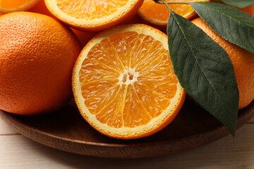 Fresh ripe oranges and leaves on light wooden table, closeup