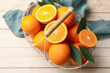 Fresh ripe oranges and leaves in basket on light wooden table, top view