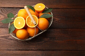 Fresh ripe oranges and leaves in basket on wooden table, top view. Space for text