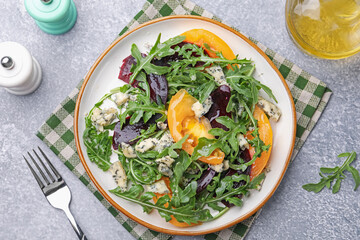 Tasty salad with arugula, blue cheese and vegetables on grey textured table, flat lay