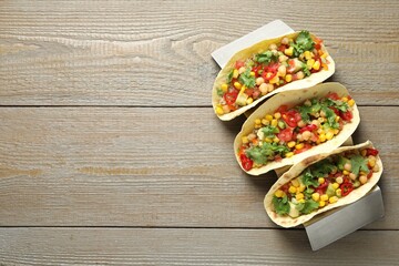Tasty vegetarian tacos with chickpeas, corn and quinoa served on wooden table, top view. Space for...