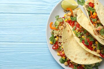 Tasty vegetarian tacos with chickpeas, corn and quinoa served on light blue wooden table, top view. Space for text