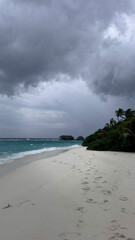 Footprints on tropical beach under stormy sky — dramatic coast and weather concept
