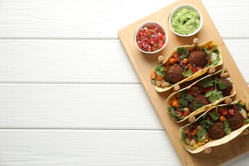 Tasty vegetarian tacos with falafel served with salsa and guacamole on white wooden table, top view. Space for text