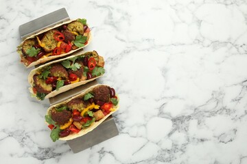 Tasty vegetarian tacos with falafel, tofu, beans and vegetables on white marble table, top view....