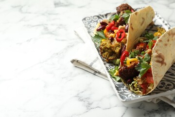 Tasty vegetarian tacos with falafel, tofu, beans and vegetables on white marble table, closeup....