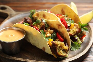 Tasty vegetarian tacos with falafel served with sauce on table, closeup