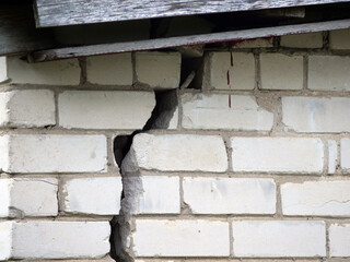 Building crack damage - large vertical crack in a white brick wall, indicating structural damage...