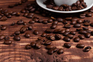 Roasted coffee beans on a wooden surface close to a coffee cup.
