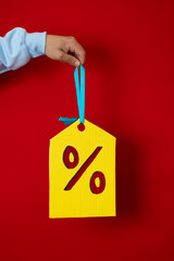 Male hand in a blue sweatshirt holding a huge yellow discount tag with his finger on a red...