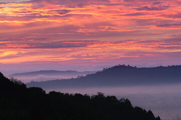 a picturesque sunrise landscape, with silhouettes of hills against a vibrant sky filled with shades of red, orange, and purple. The foreground features a dark silhouette of trees