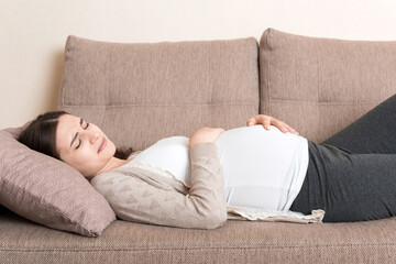 Pregnant woman with painful belly on sofa at home